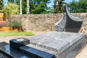 Monument funéraire moderne en granit gris sculpté exposé en extérieur.